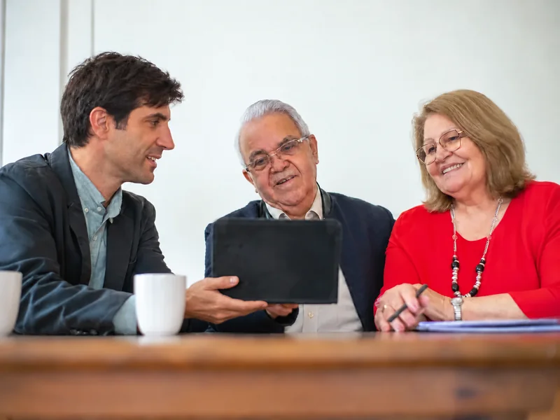 An adviser discusses information on a tablet with a couple at a table.